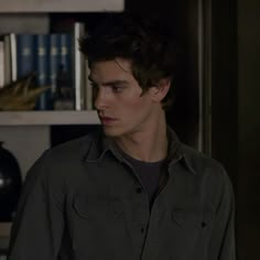 a young man standing in front of a bookshelf