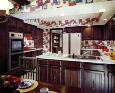 a large kitchen with wooden cabinets and white counter tops is decorated with red, blue, and yellow wallpaper