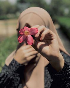 a woman holding a flower up to her face while wearing a hijab and looking at the camera