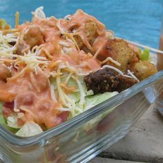 a salad in a plastic container with meatballs and cheese on it next to a swimming pool