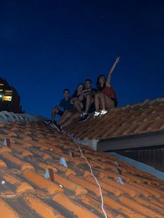 four people are sitting on the roof of a building at night, with their arms in the air