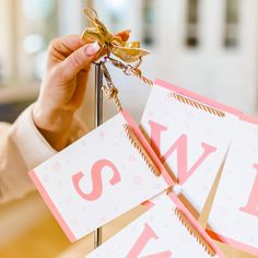 a person holding up two small cards with the letter s on them and a gold bow