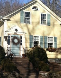 a yellow house with blue shutters and a wreath on the front door is shown