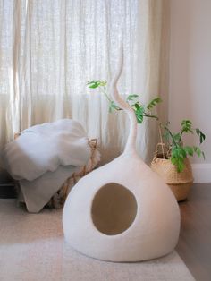 a white vase with a plant in it sitting on the floor next to a window