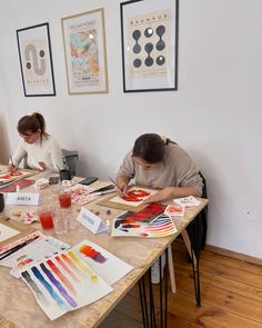 two people are sitting at a table with art supplies on it and one person is painting