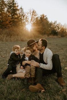 a man, woman and two children are sitting on the grass in an open field