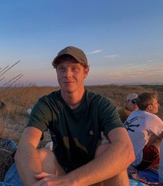 a man sitting on top of a blue blanket next to a tall grass covered field