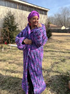 a woman standing in the grass wearing a purple knitted cardigan and black boots