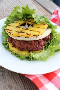 a hamburger with lettuce and pineapple slices on it sitting on a white plate