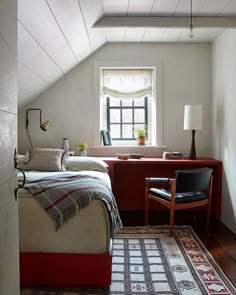 a bed sitting under a window next to a chair and desk in a room with white walls