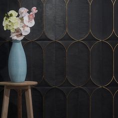 a blue vase with white and pink flowers on a stool in front of a black wall