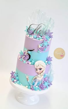 a three tiered cake decorated with frozen princesses and snowflakes on top