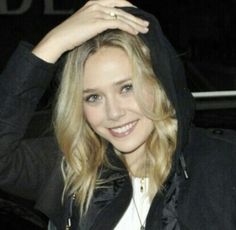 a woman in a black jacket is smiling and holding her hands up to her head