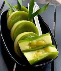 sliced green fruit on a black plate with chopsticks