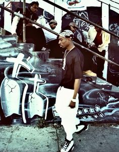 a young man standing in front of graffiti on the side of a building next to stairs