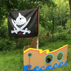 a pirate ship made out of cardboard sitting in the grass next to a black flag