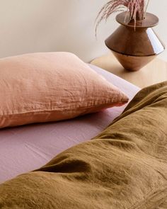 a pink pillow sitting on top of a bed next to a vase with a plant