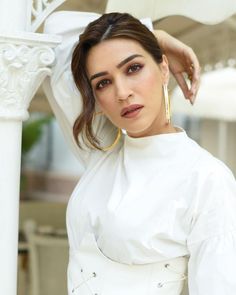 a woman posing for the camera with her hand on her head and wearing a white top