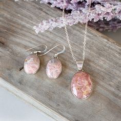 three necklaces and earring sets with pink flowers in the background on a piece of wood