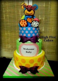 a three tiered cake with a teddy bear on top and welcome baby written on the bottom