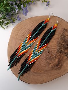 two pairs of beaded earrings sitting on top of a wooden board next to flowers