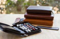 two leather cases with pens and pencils in them sitting on a table next to each other