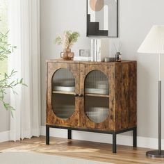 a wooden cabinet with glass doors in a living room next to a lamp and pictures on the wall