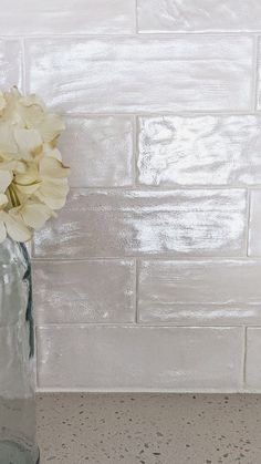 white flowers in a clear glass vase against a white brick wall with speckles