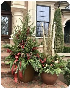 two potted plants sitting on top of a brick walkway next to a house with christmas decorations