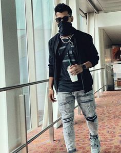 a man in ripped jeans and a black hoodie is holding a coffee cup while wearing a mask