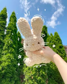 a person holding up a stuffed animal in front of some trees and blue sky with white clouds