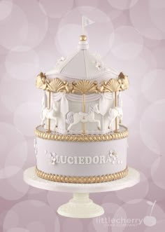 there is a white and gold carousel cake on top of a stand with pink bubbles in the background