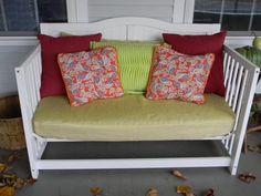 a white bench with pillows on it in front of a window and leaves all around