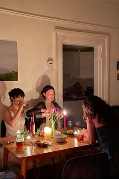 three women sitting at a table with candles in front of them and one woman standing behind the table