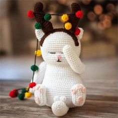 a crocheted white bunny sitting on top of a wooden table next to a string of lights