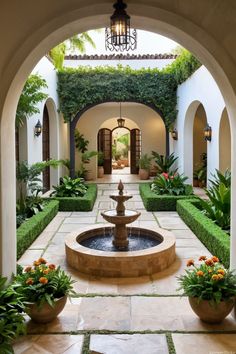 a courtyard with a fountain surrounded by greenery and potted plants on either side