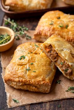 two meat filled pastries sitting on top of a piece of wax paper next to a dish