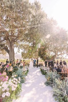 an outdoor ceremony with flowers and greenery on the aisle, surrounded by people sitting at tables