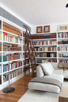 a living room filled with lots of books and furniture next to a tall book shelf