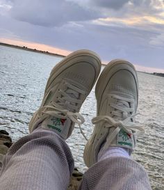 someone's feet wearing tennis shoes by the water