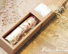 two rolls of paper in a box on a wooden table next to dried flowers and baby's breath