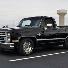 a black pickup truck parked in a parking lot next to a water tower on a cloudy day