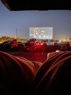 cars parked in a parking lot at night with a movie on the wall behind them