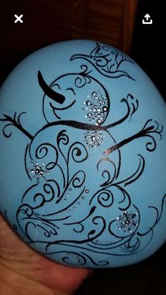 a hand holding a blue painted rock with black and white designs on it's face