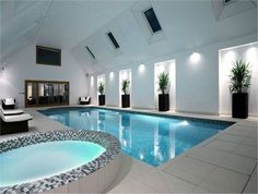 an indoor swimming pool in a large room with white walls and tiled flooring, surrounded by potted plants