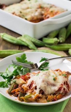 a white plate topped with lasagna covered in sauce and vegetables next to a casserole dish