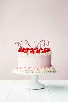 a pink cake with cherries and white frosting on a pedestal against a pink background