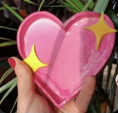 a hand holding a pink heart shaped box with yellow stars on the top and bottom