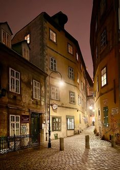 an empty cobblestone street at night with buildings in the background