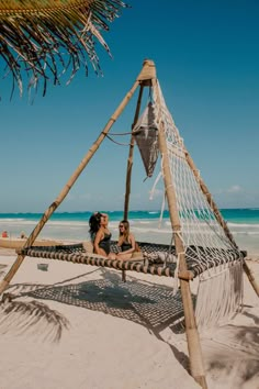 two women are sitting in a hammock on the beach, one is kissing